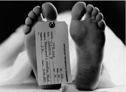 The tagged toe of a dead body is in focus as the covered body lays atop a table.