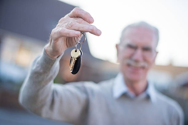 Senior man holding keys to a house - real estate concepts